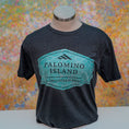 Load image into Gallery viewer, Black t-shirt with 'Palomino Island' logo on a mannequin against a colorful abstract background